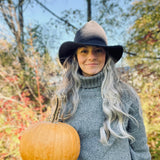 Owner Olivia Ashline in a North Ferry Packable Sun Hat, in Ash, Pointed and Styled into a Witches Hat shape, posed outside in fall Foliage and pumpkin patch