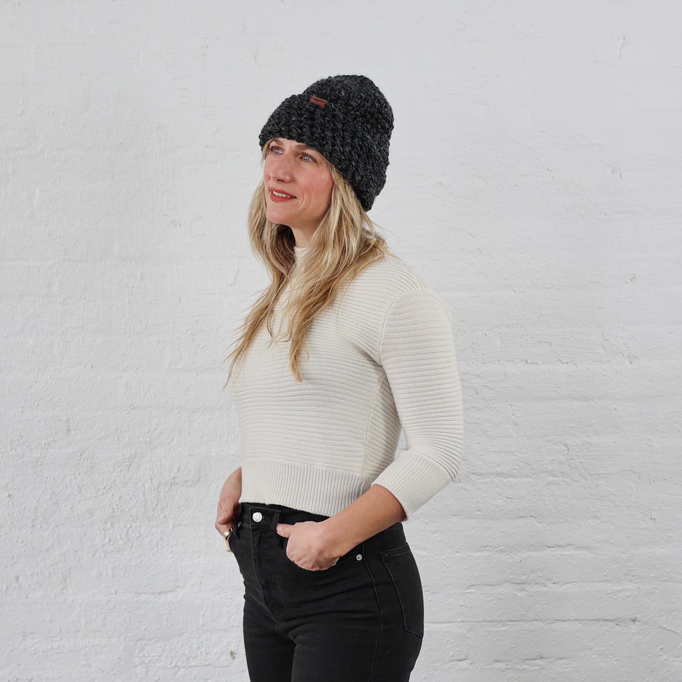 Woman styled charcoal winter beanie that is chunky knit, folded up with a thick cuff.