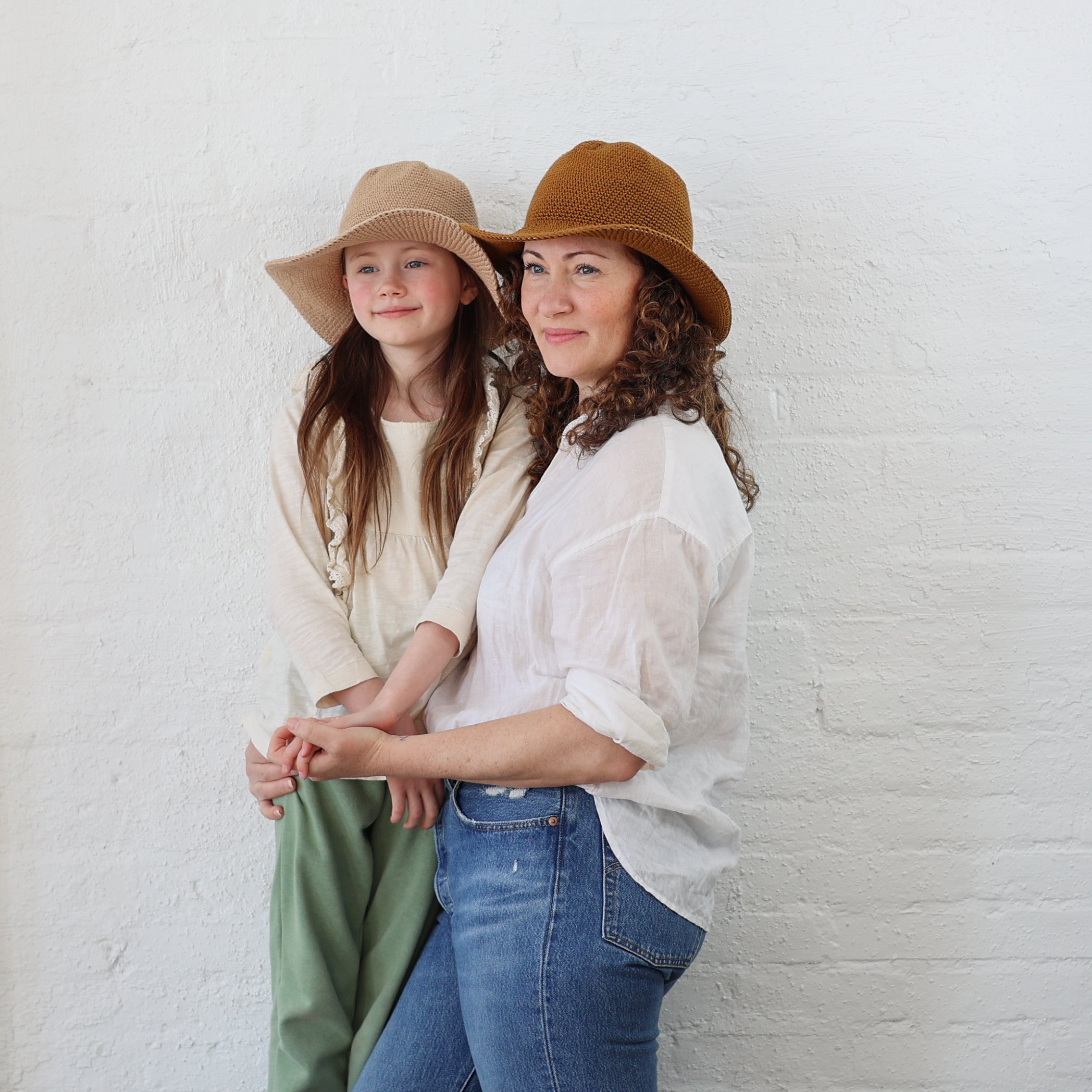 A Mother and a Daughter wearing matching packable North ferry sun hats, one in nude nativo and the other in sand.  Both hats are the same style/universal size, and both fit kid and Adult sizes