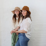 A Mother and a Daughter wearing matching packable North ferry sun hats, one in nude nativo and the other in sand.  Both hats are the same style/universal size, and both fit kid and Adult sizes