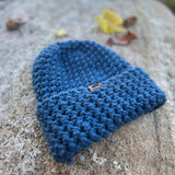 Blue knitted beanie on a rock with a blurred natural background