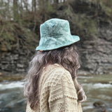 Person wearing a green patterned bucket hat a reversible Sun hat in recycled prints