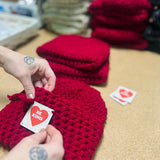 Red knitted items with 'Be Kind' cards on a table