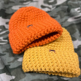 Spice and Gold colored beanies in High Vis Colors and layered in a bundle over camo fabric