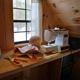 Sewing setup in a wood tiny house overlooking snowy woods scene. Sewing Bucket Hats in February for a sustainable hat company, available in spring reversible waterproof bucket hats and PACKABLE Sun hats made in the finger lakes
